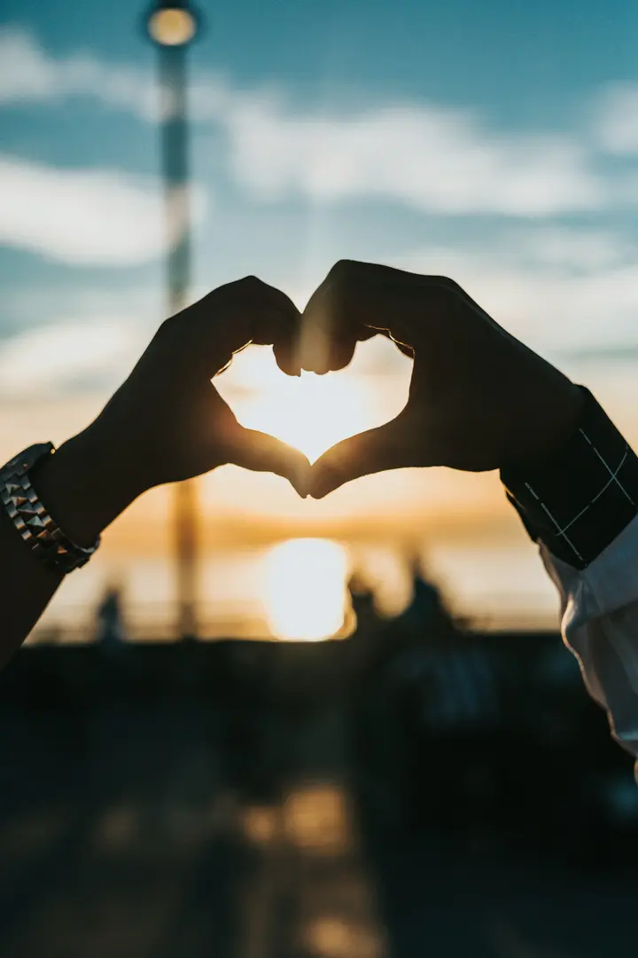 Due mani formano un cuore contro un tramonto